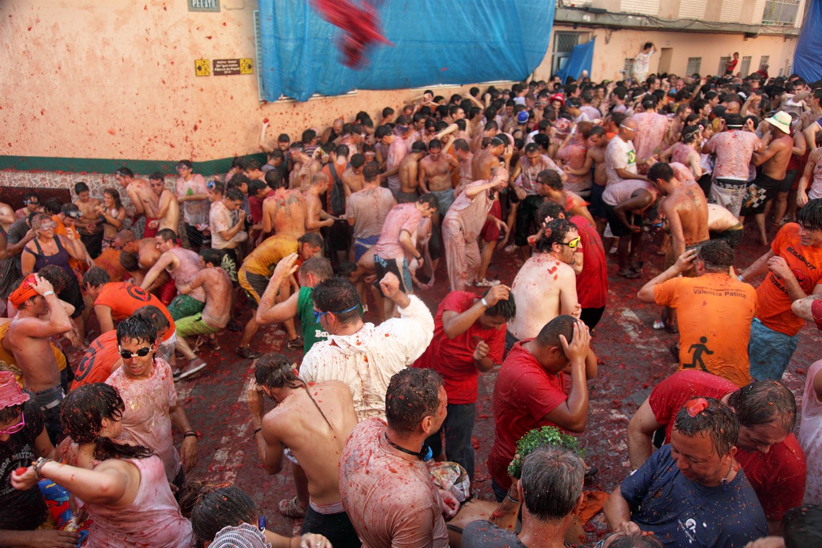 A crowd covered in red tomato pulp packed into a narrow street during La Tomatina in Bunol, Spain
