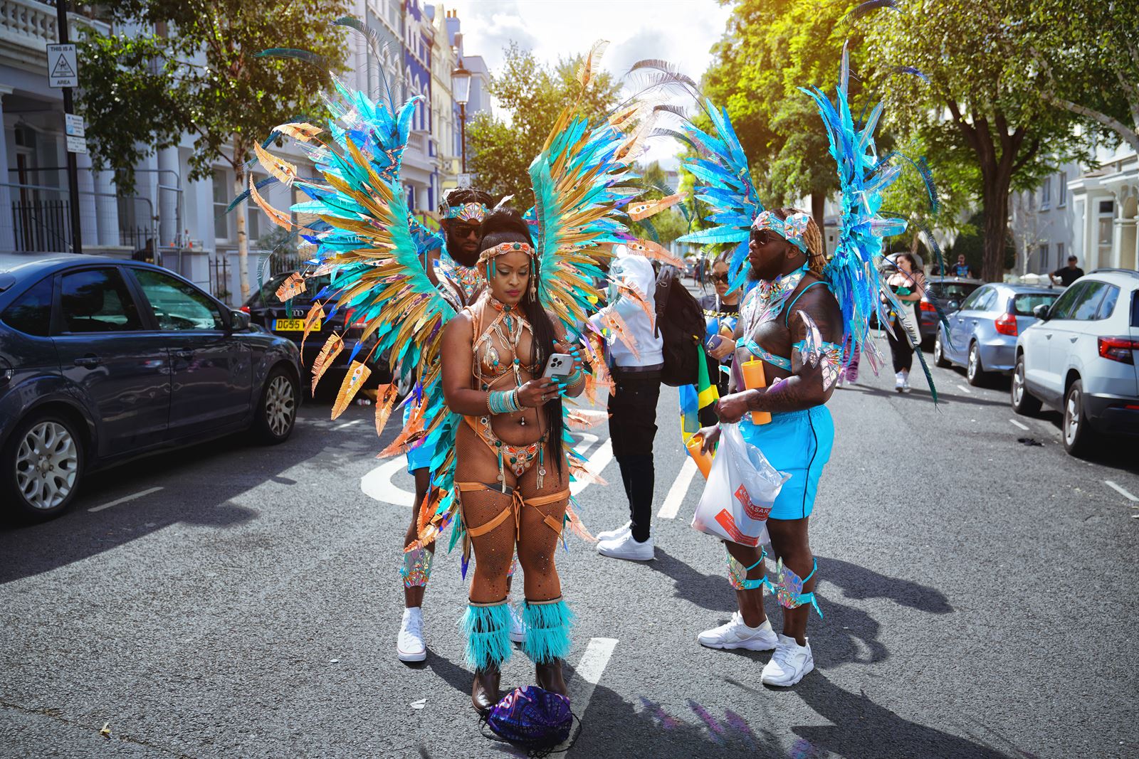 A dancer in a vivid feathered costume leads the parade through a packed west London street at Notting Hill Carnival