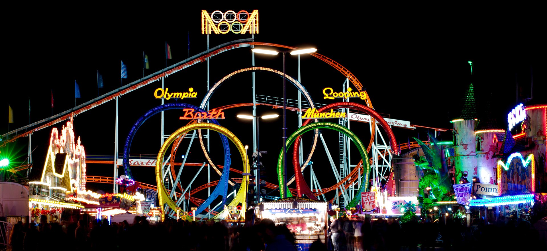 The Oktoberfest fairground in Munich lit up at night, with the looping roller coaster glowing against the dark sky